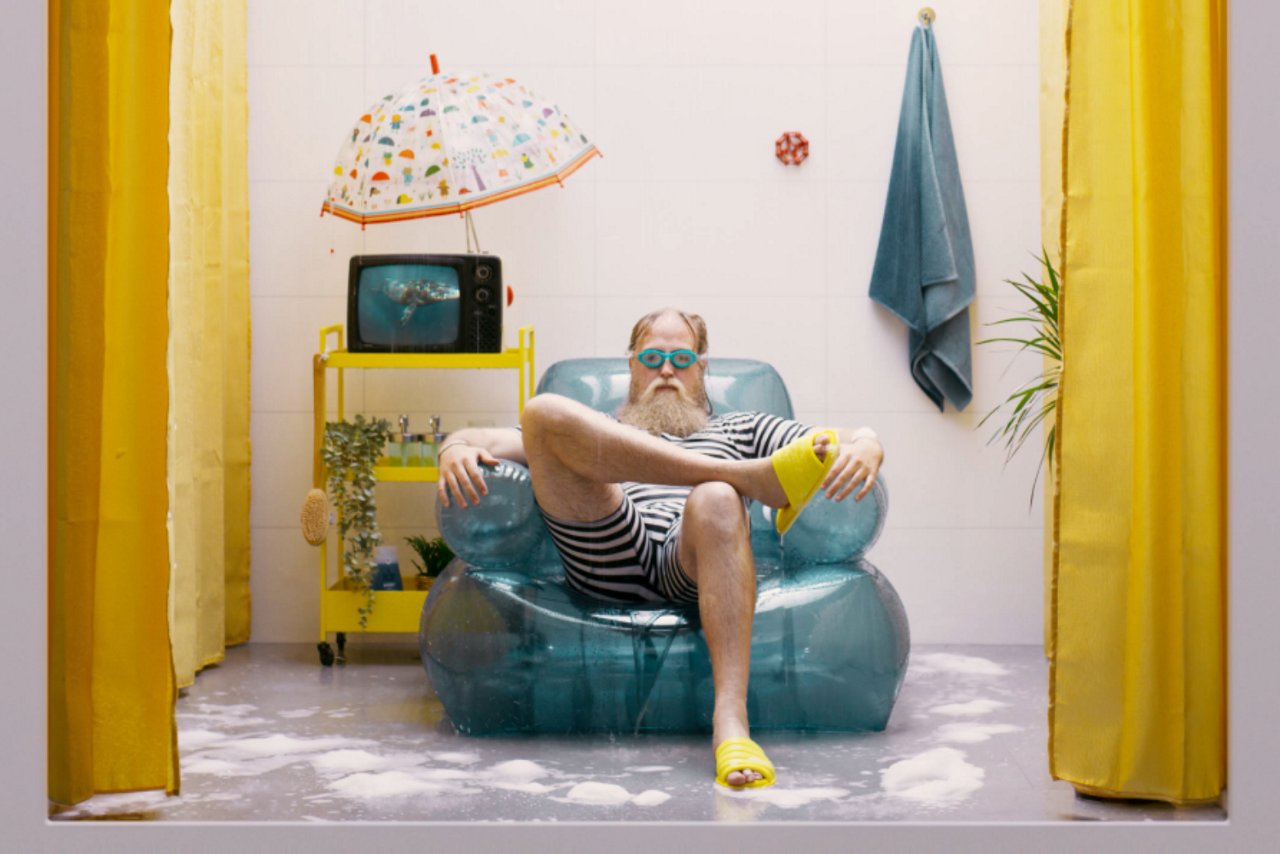 En mann som har på seg dykkebriller, mens han sitter avslappet i en oppblåsbar stol inne i en dusj.