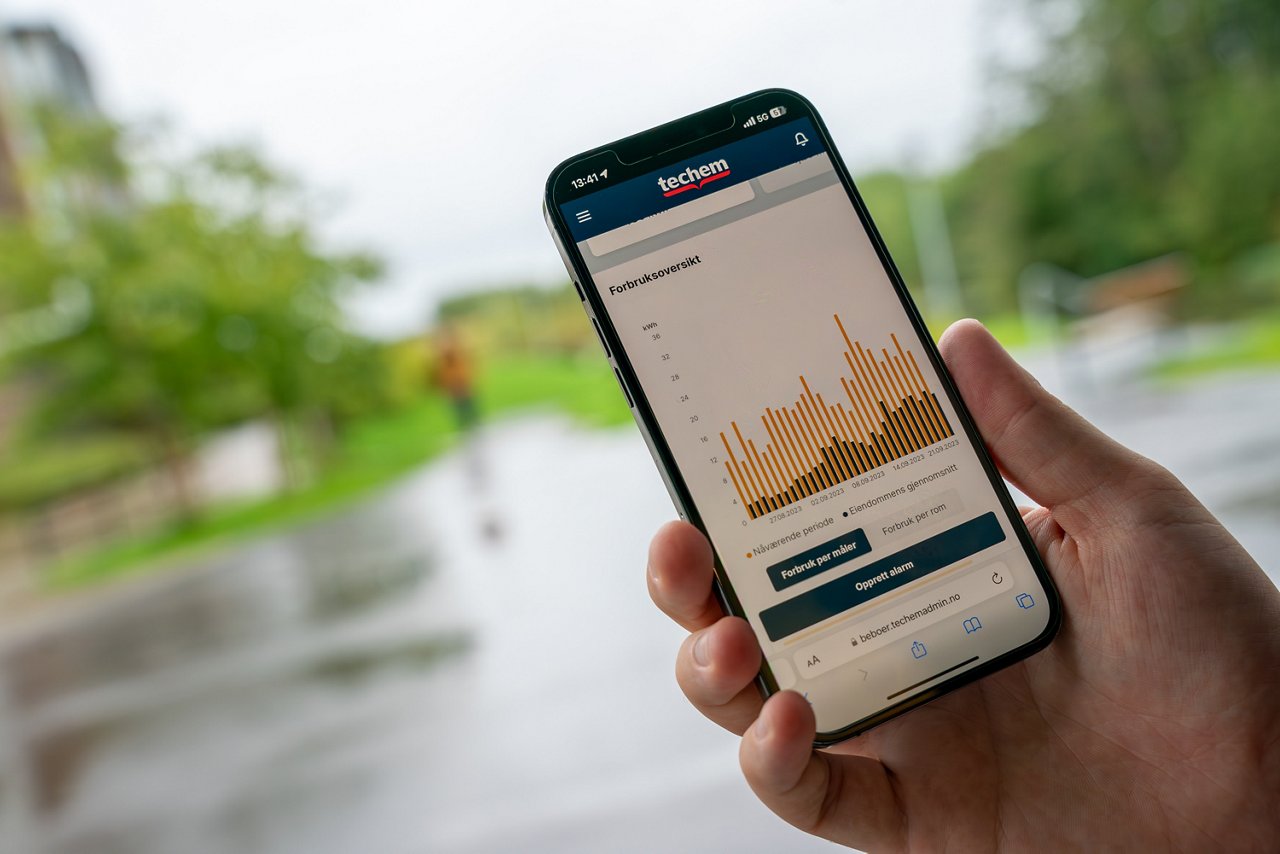 En person holder en iphone, på skjermen ser man Techem Beboer App.