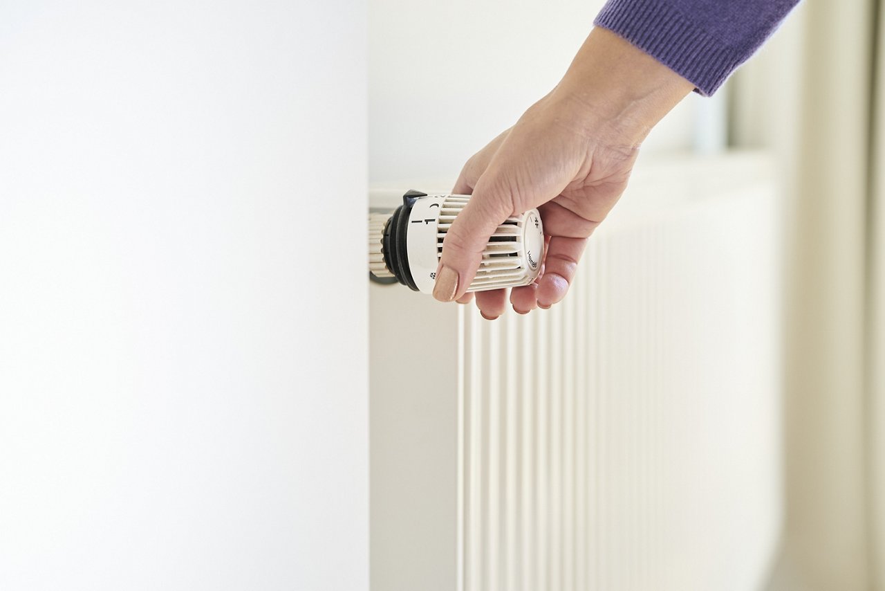 alt-Text: Hand stellt Thermostaat an Heizung ein