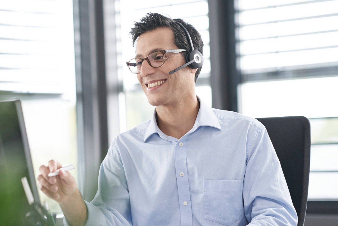 Mand, der sidder ved computer med headset på. 