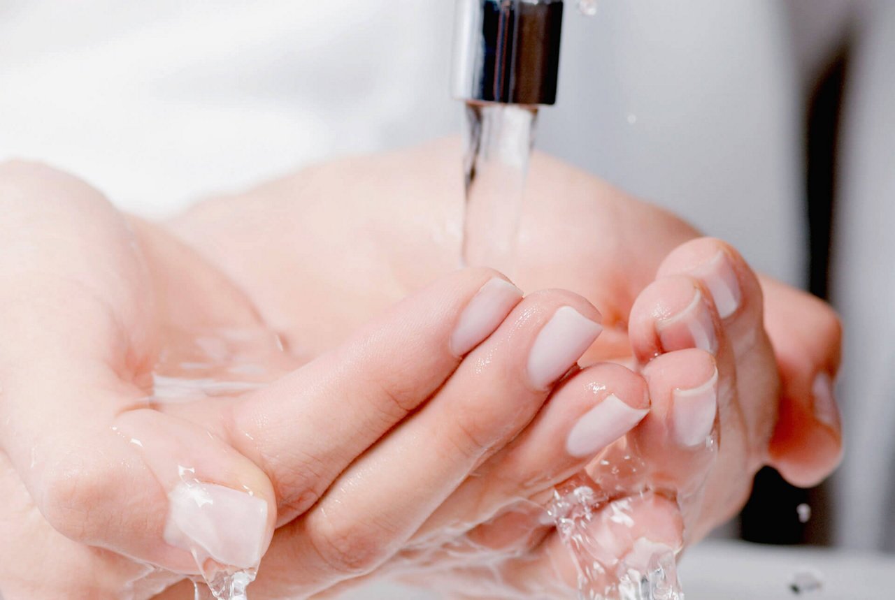 Eine Person hält die Hände unter einen laufenden Wasserhahn. 