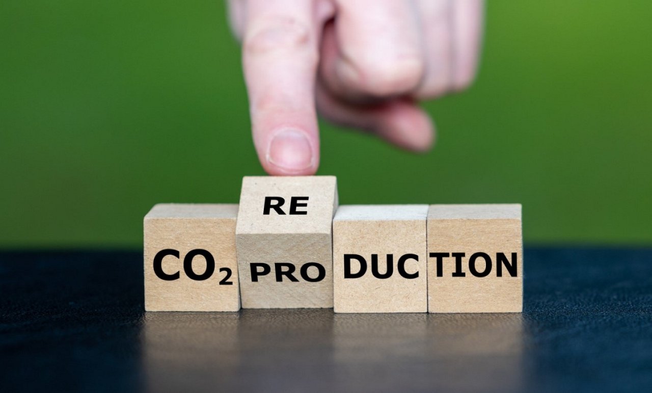  Eine Hand dreht einen Holzblock, um das Wort "CO₂ Production" in "CO₂ Reduction" zu ändern. 