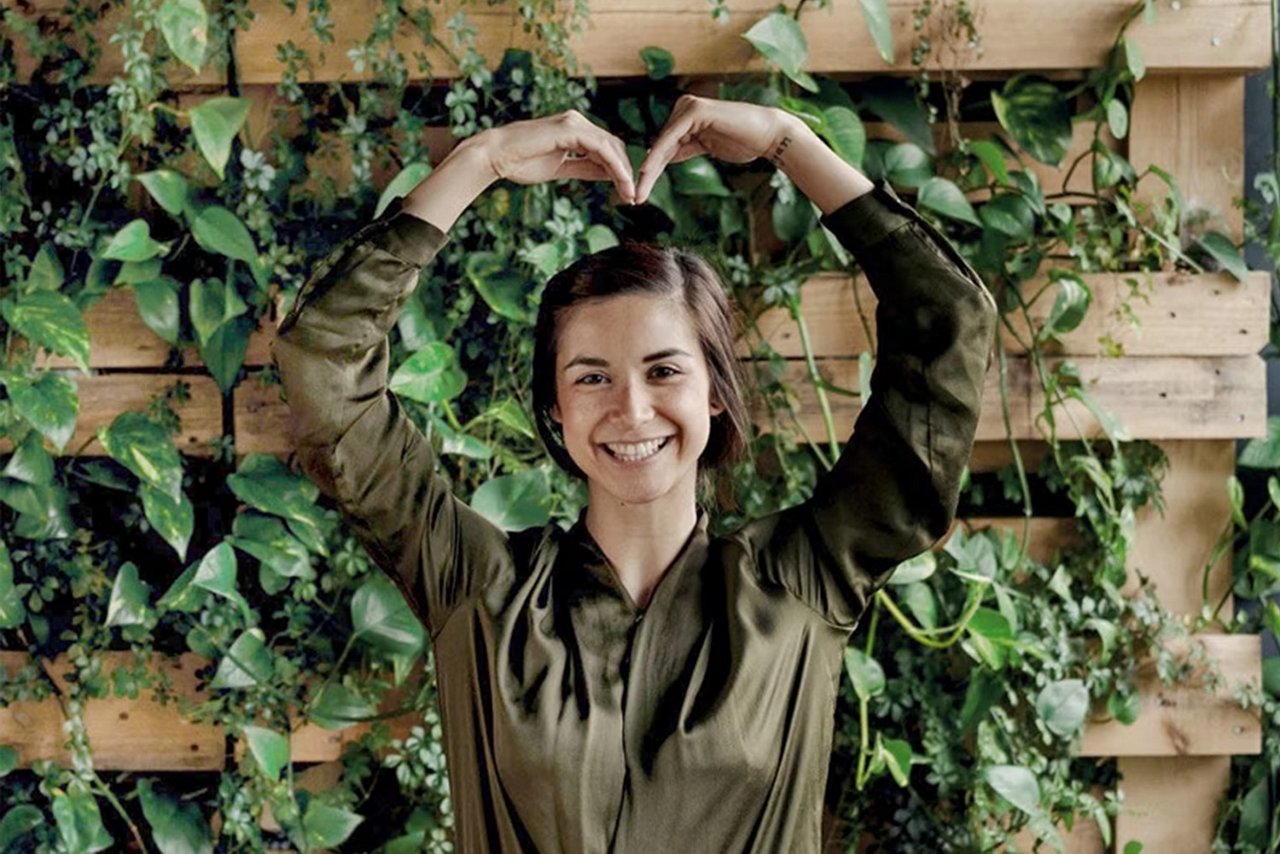 Kvinde står foran væg med grønne blade. 