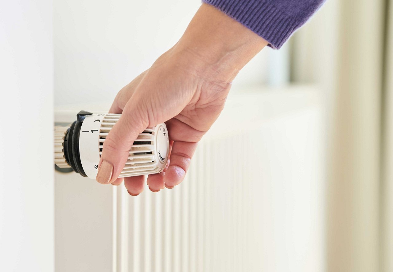 Une main tourne un régulateur de chauffage blanc.