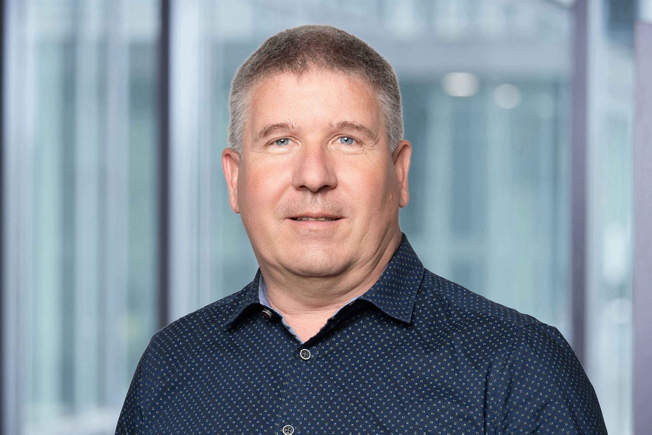 Photo Conseiller de vente Administrations G. Hofmann Région Suisse romande devant un arrière-plan de bureau flou.