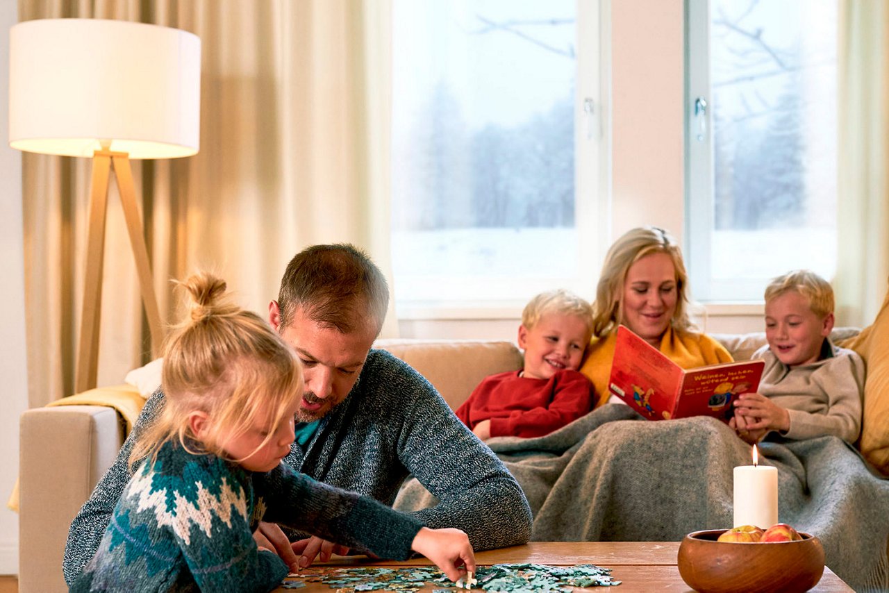Familie med tre børn spiller og sidder i en sofa i stuen. 