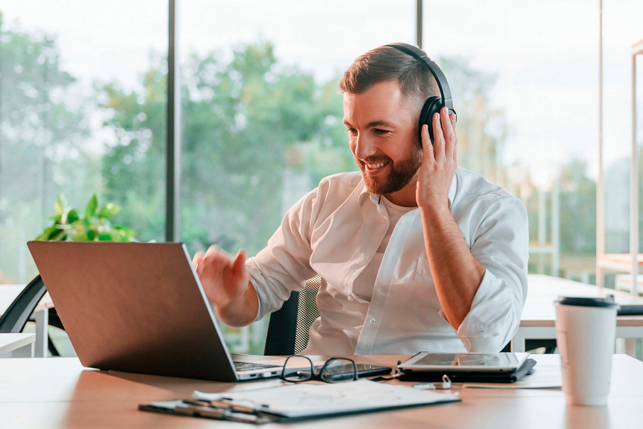 Mand sidder ved sit kontorbord med headphones og laptop. 