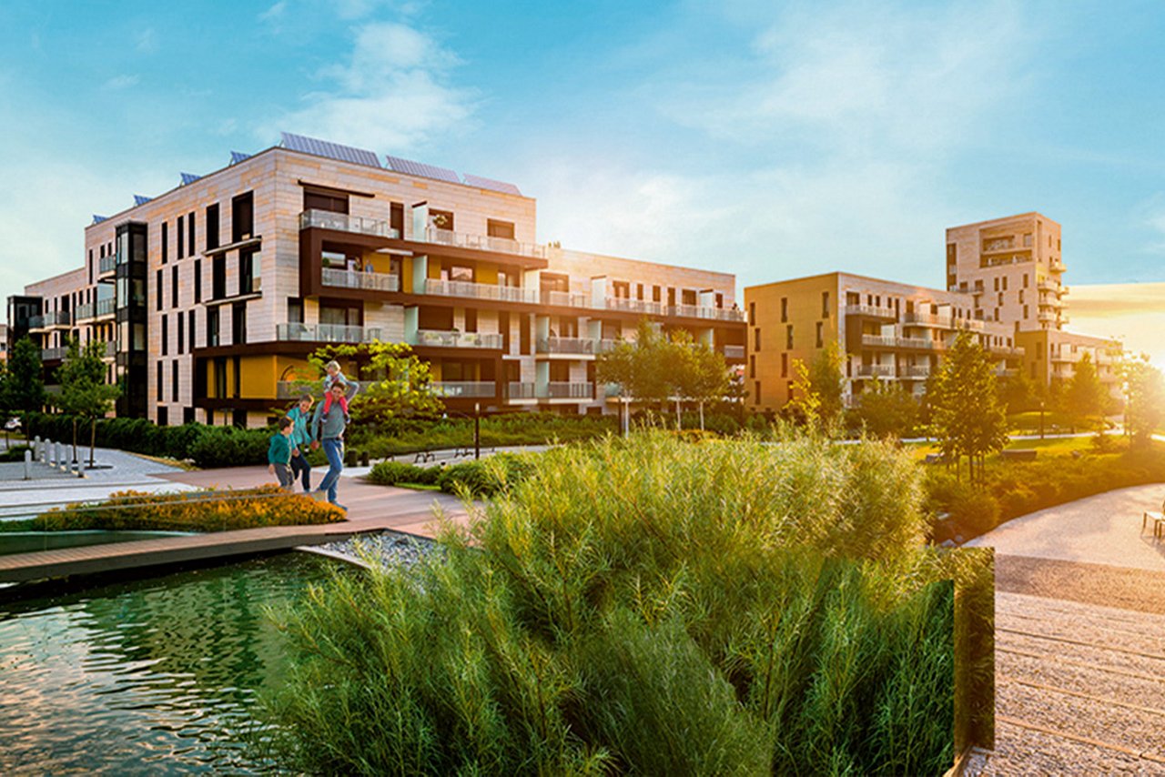 Familie går foran bygninger i grønt miljø. 