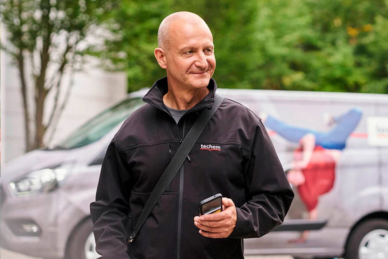 Mand med jakke med Techem logo står foran firmabil. 