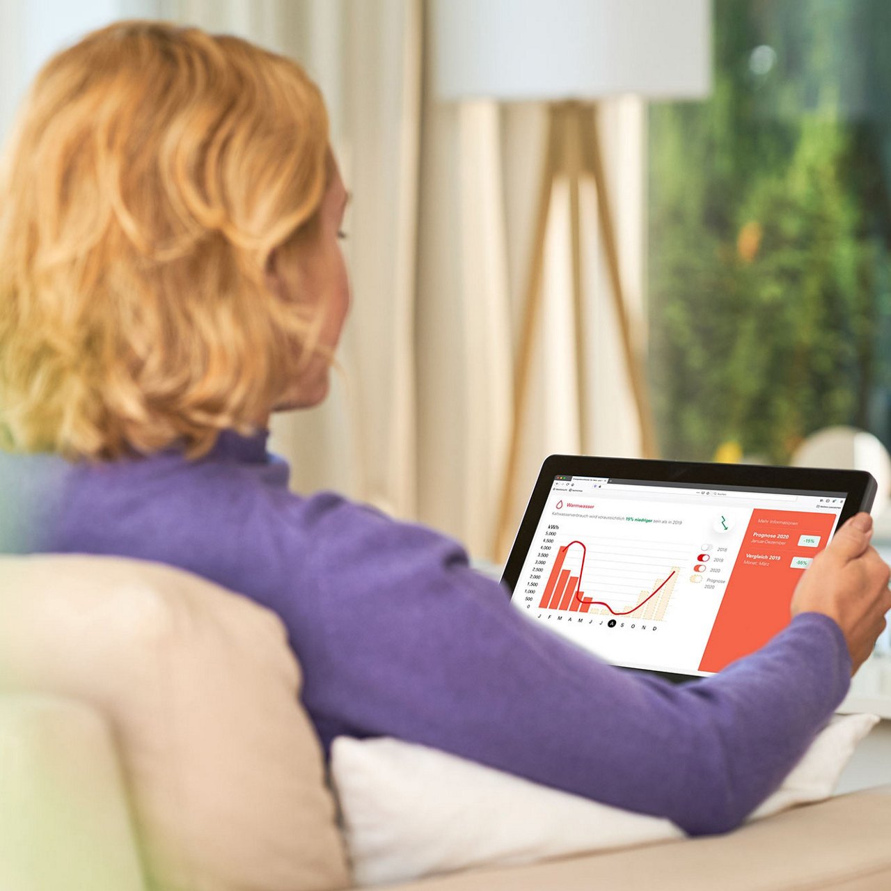  Eine Frau sitzt auf dem Sofa und betrachtet ein Tablet mit einem Diagramm auf dem Bildschirm.