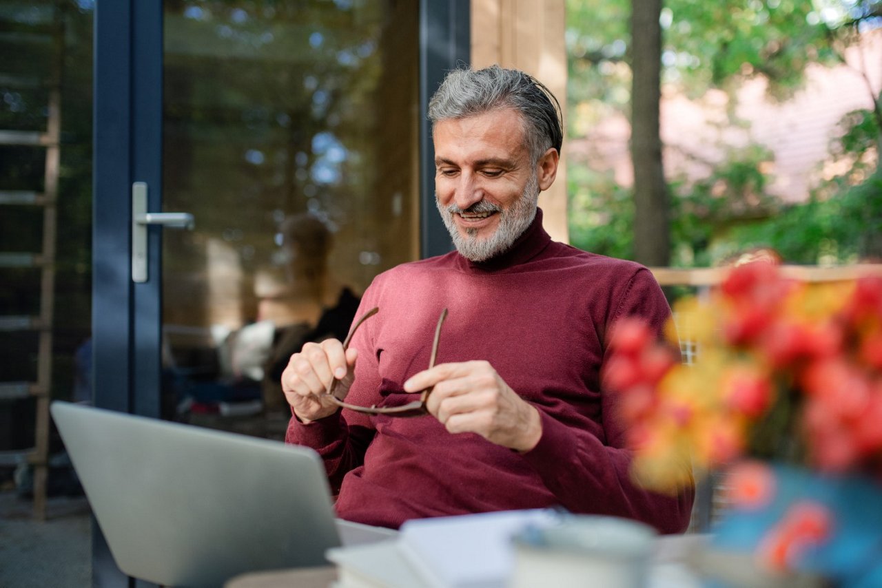Mann sitzt auf Terrasse und schaut auf seinen Laptop