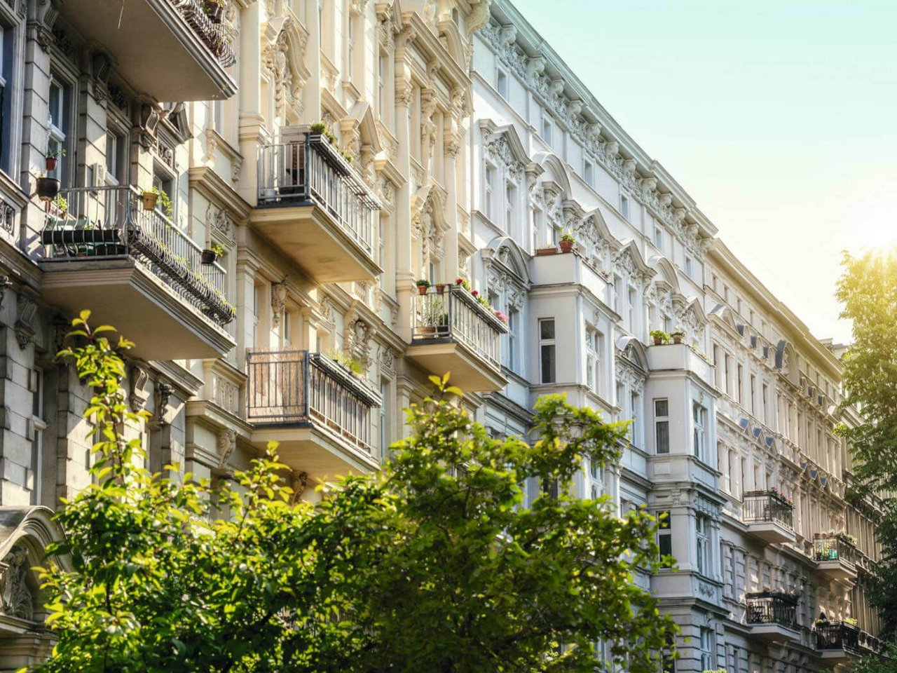 Fassade eines historischen Wohnhauses mit Balkonen und grünen Bäumen im Vordergrund bei Tageslicht