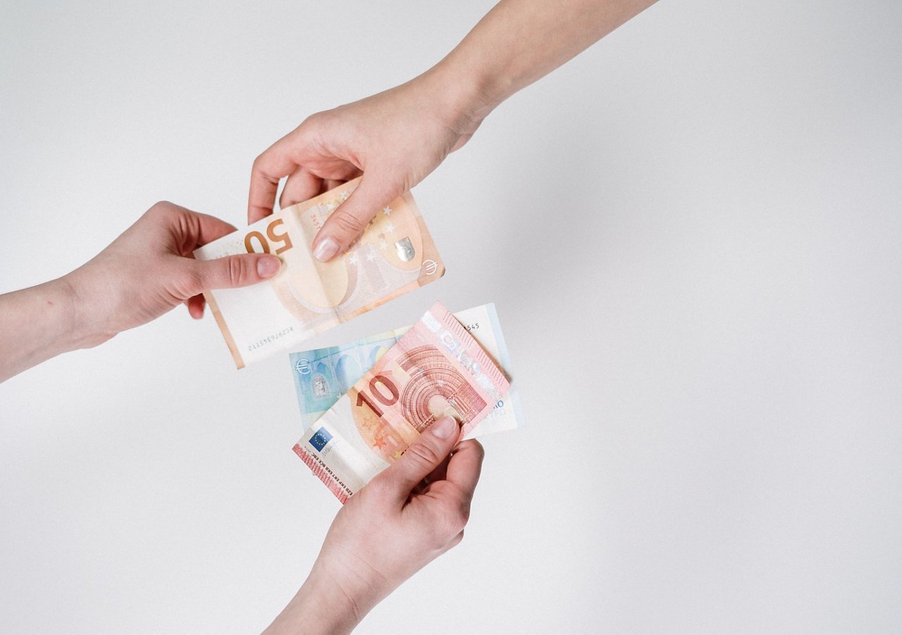 Zwei Hände übergeben sich mehrere Euro-Banknoten. Eine Hand gibt Scheine in verschiedenen Werten, während die andere sie entgegennimmt