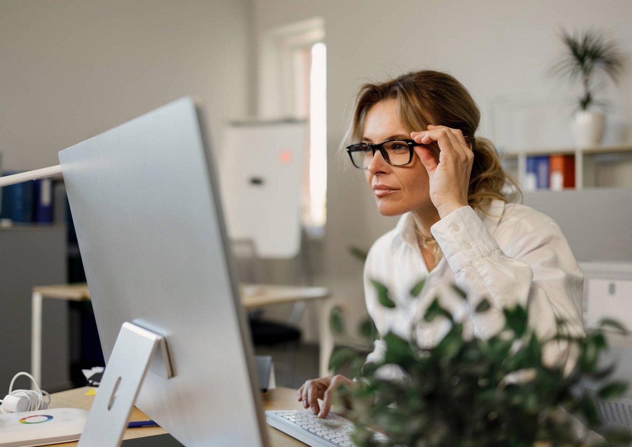 Frau mit Brille konzentriert vor großem Computerbildschirm im Büro