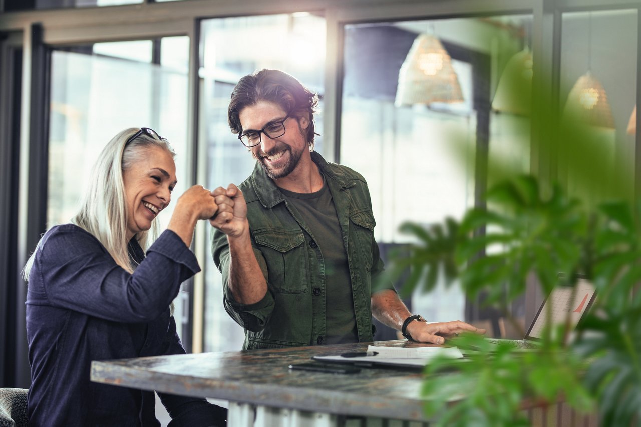 Young businessman and senior businesswoman making a fist bump at office. Business colleagues looking happy and excited after completion of project.