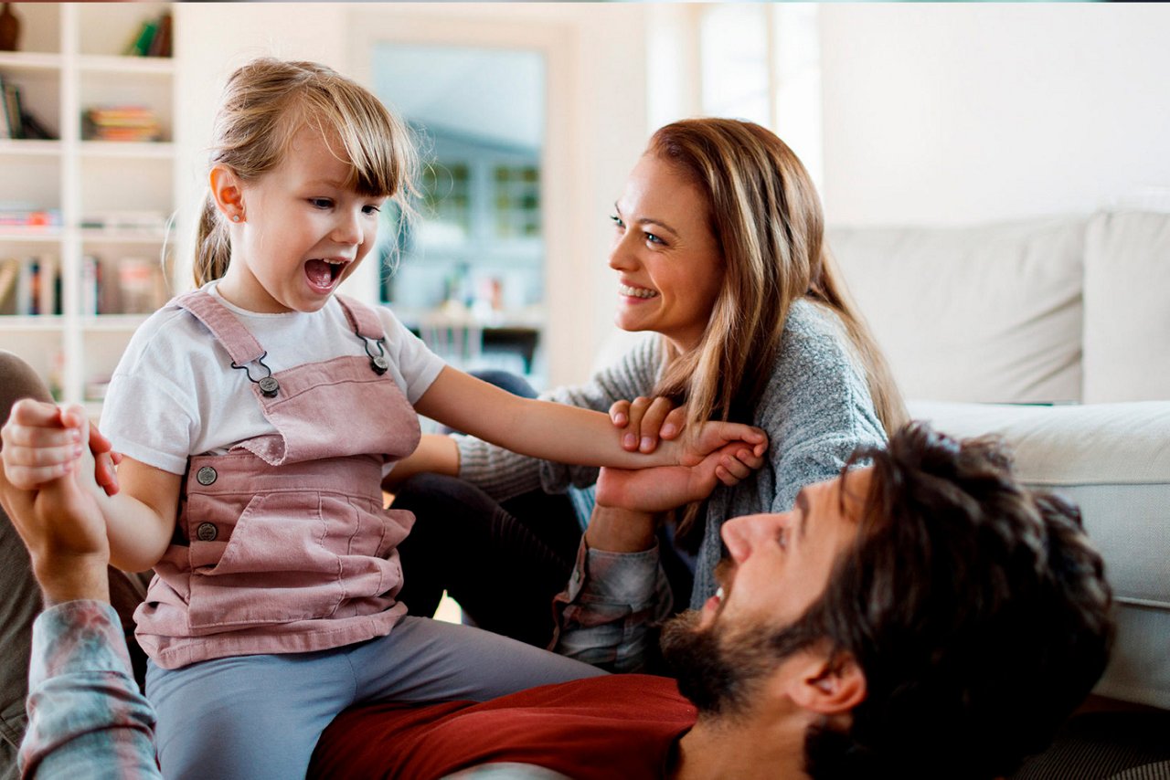 Familie på tre er i stuen ved sofaen. 