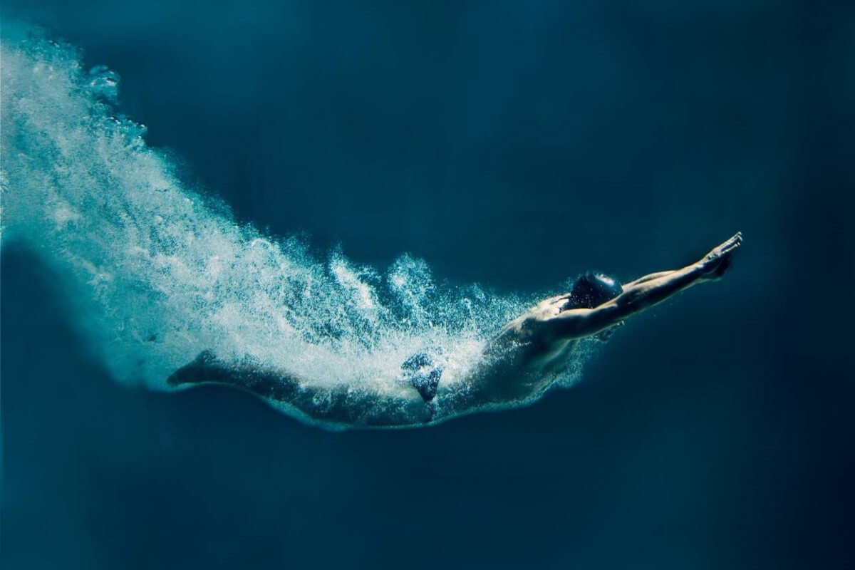 Ein Schwimmer taucht mit voller Geschwindigkeit ins Wasser ein, umgeben von aufsteigenden Blasen.
