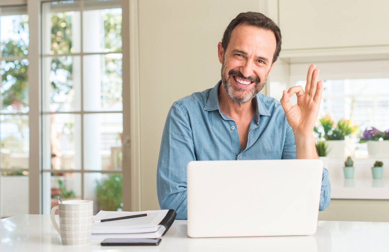 Middle age man using laptop at home doing ok sign with fingers, excellent symbol; Shutterstock ID 1129938431; purchase_order: TE/2024/001 Diverses Q1 ; job: TE/2024/001 Diverses Q1; client: Techem Energy Services GmbH und mit ihr gemäß §§ 15 ff AktG verbundene Unternehmen; other: bestellt von Vittoria