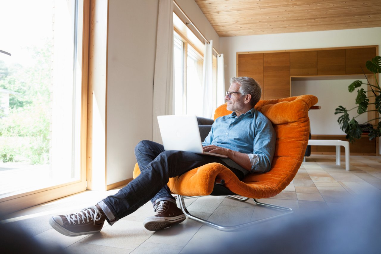 Mann mit Brille sitzt auf Sessel mit Laptop