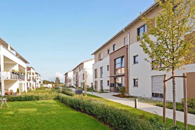  Moderne Wohnsiedlung mit Mehrfamilienhäusern und viel Rasen sowie ein paar Bäumen.