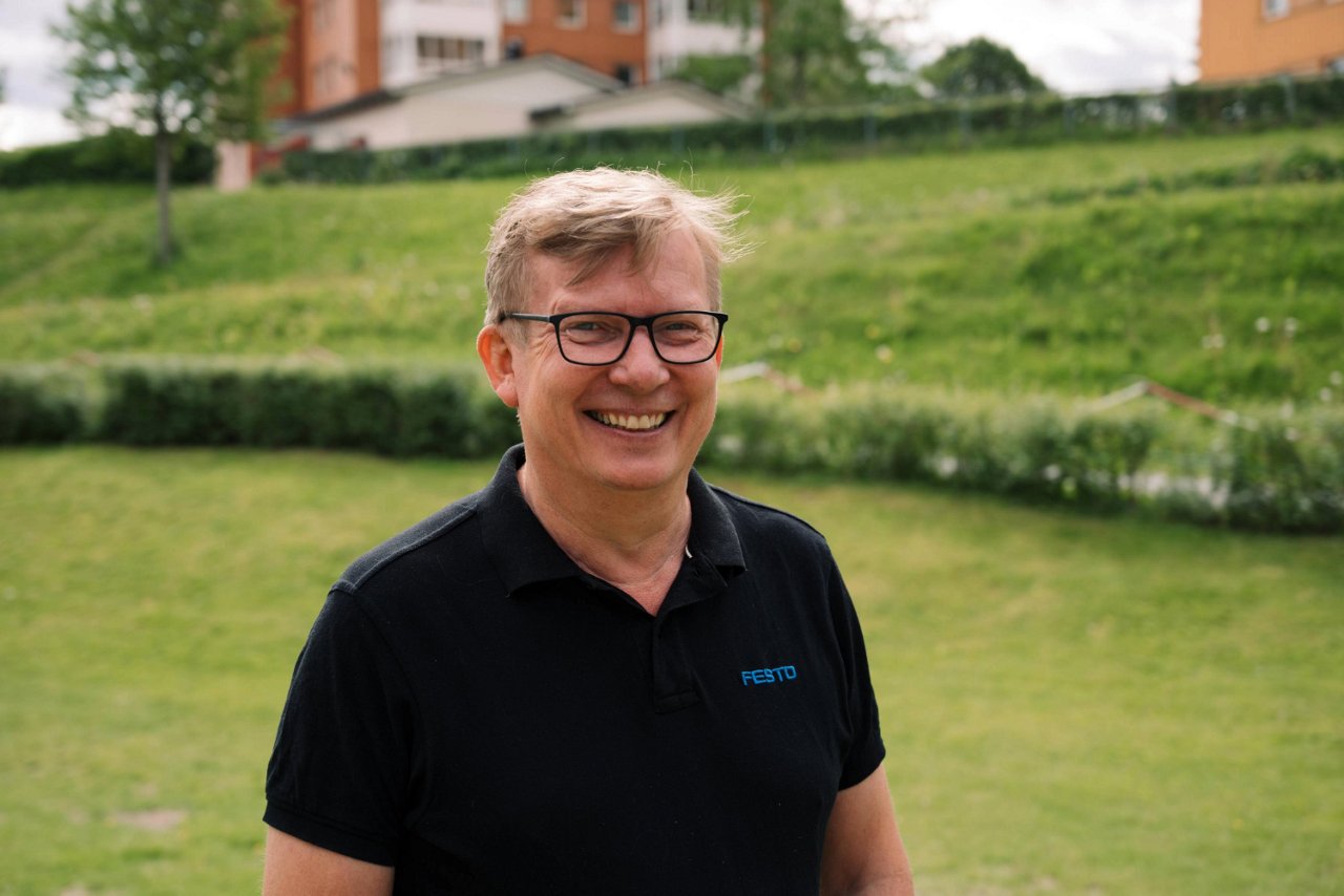 En mann med biller smiler imens han står på en gressplen.