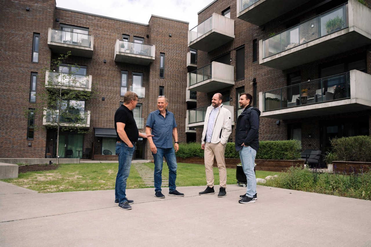 Personer som står og snakker foran en boligblokk, bygningen er  laget av murstein, som gir den et klassisk og solid utseende.