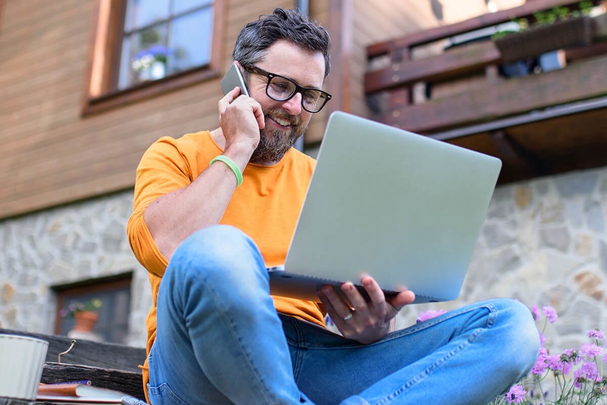 Mann mit Laptop und Handy sitzt draußen vor dem Haus und arbeitet.   Links unten steht „Techem Immo Point“ auf einem roten Feld.