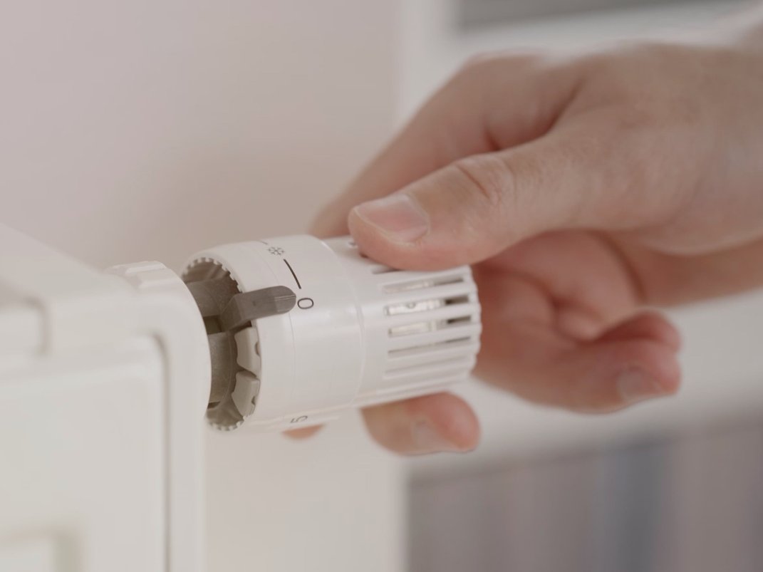 Eine Hand dreht an einem Heizkörperthermostat