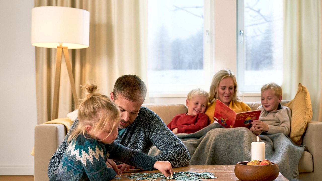 Mutter sitzt mit beiden Kindern auf dem Sofa und liest. Der Vater spielt mit der Tochter Puzzle.