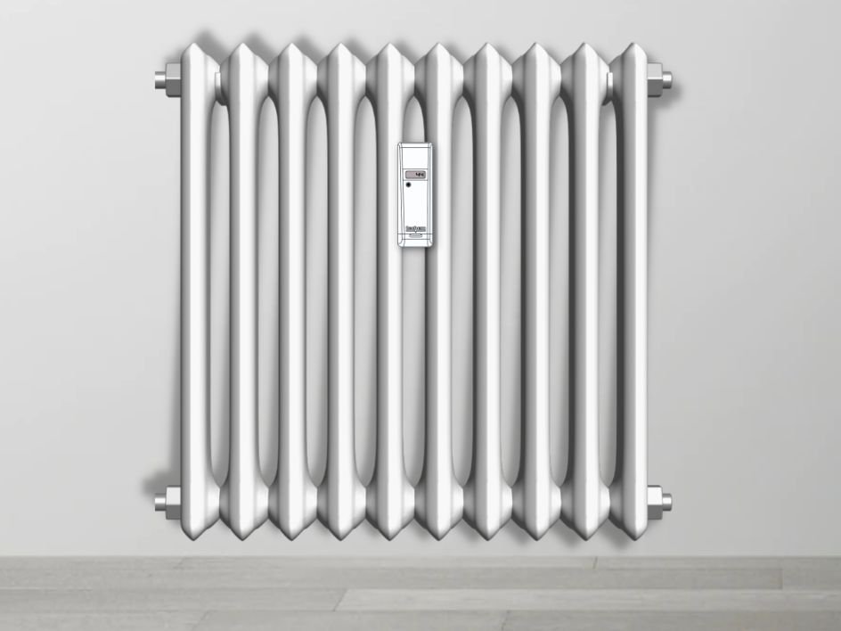 Radiador de hierro fundido de estilo clásico con múltiples columnas verticales, montado en una pared gris sobre un suelo de madera clara. El radiador tiene un acabado plateado brillante y un repartidor de costes de calefaccion blanco instalado entre  las secciones centrales.