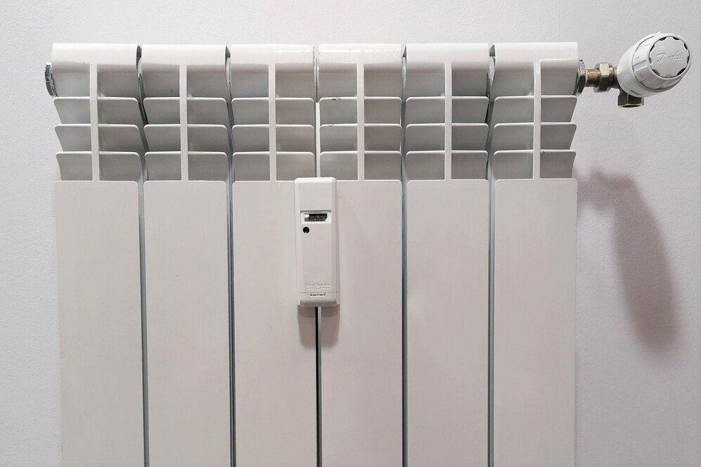 Radiador blanco de paneles verticales con una válvula termostática para el control de la temperatura en la parte superior derecha. También tiene instalado un repartidor de costes de calefacción en la parte central.