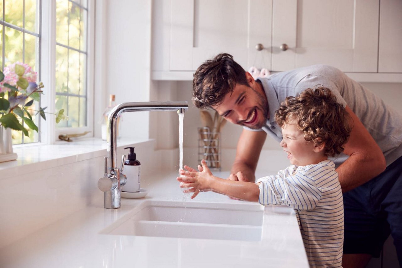 Papà e figlio che ridono mentre il bambino si sta lavando le mani nel lavandino della cucina utilizzando il sapone il sapone.