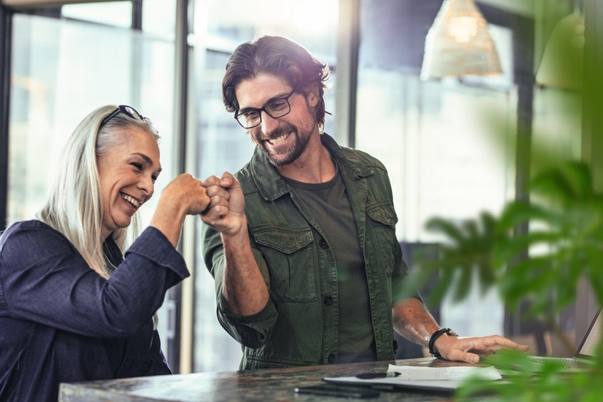 Zwei Personen geben sich einen Faustgruß in einem modernen Büro mit Pflanzen und großen Fenstern