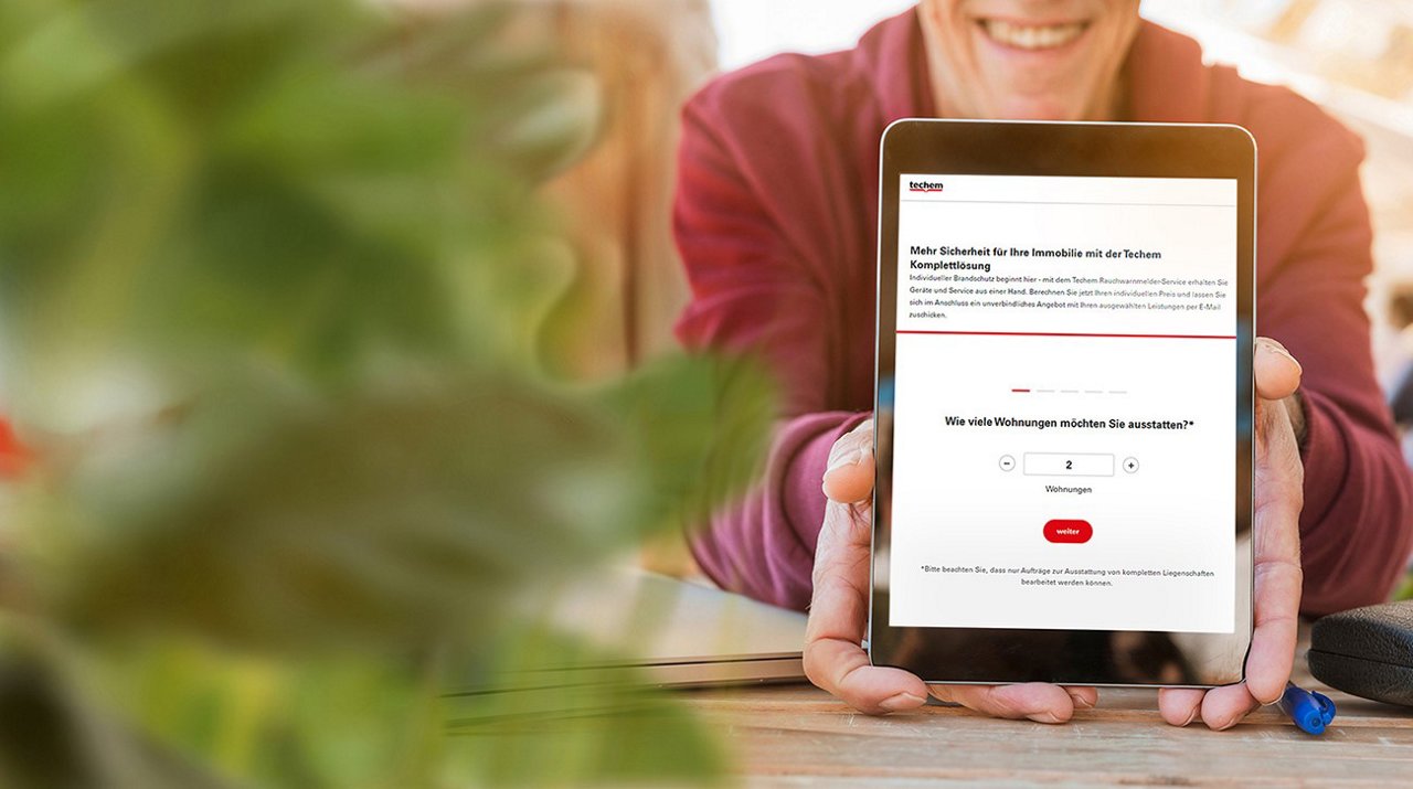 Eine Person hält ein Tablet in die Kamera, auf dem der Rauchwarnmelder-Rechner von Techem geöffnet ist.