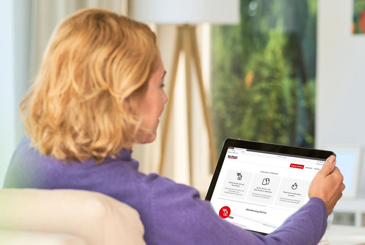 Frau sitzt im Wohnzimmer und schaut sich auf ihrem Tablet das Portal mein.techem an