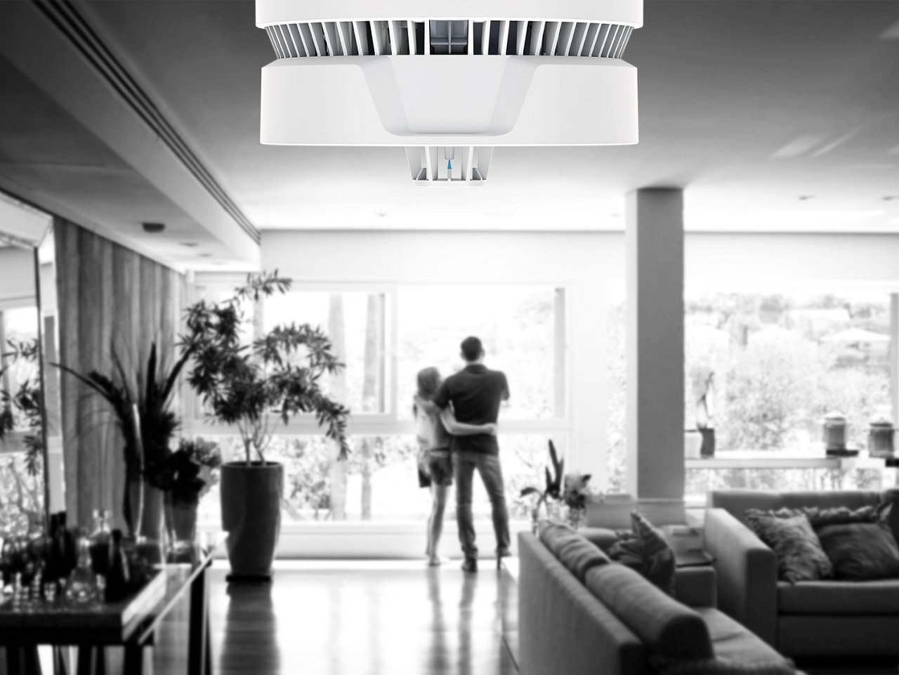 Pärchen steht im Wohnbereich am Fenster. Im Vordergrund sieht man den Multisensor Plus.