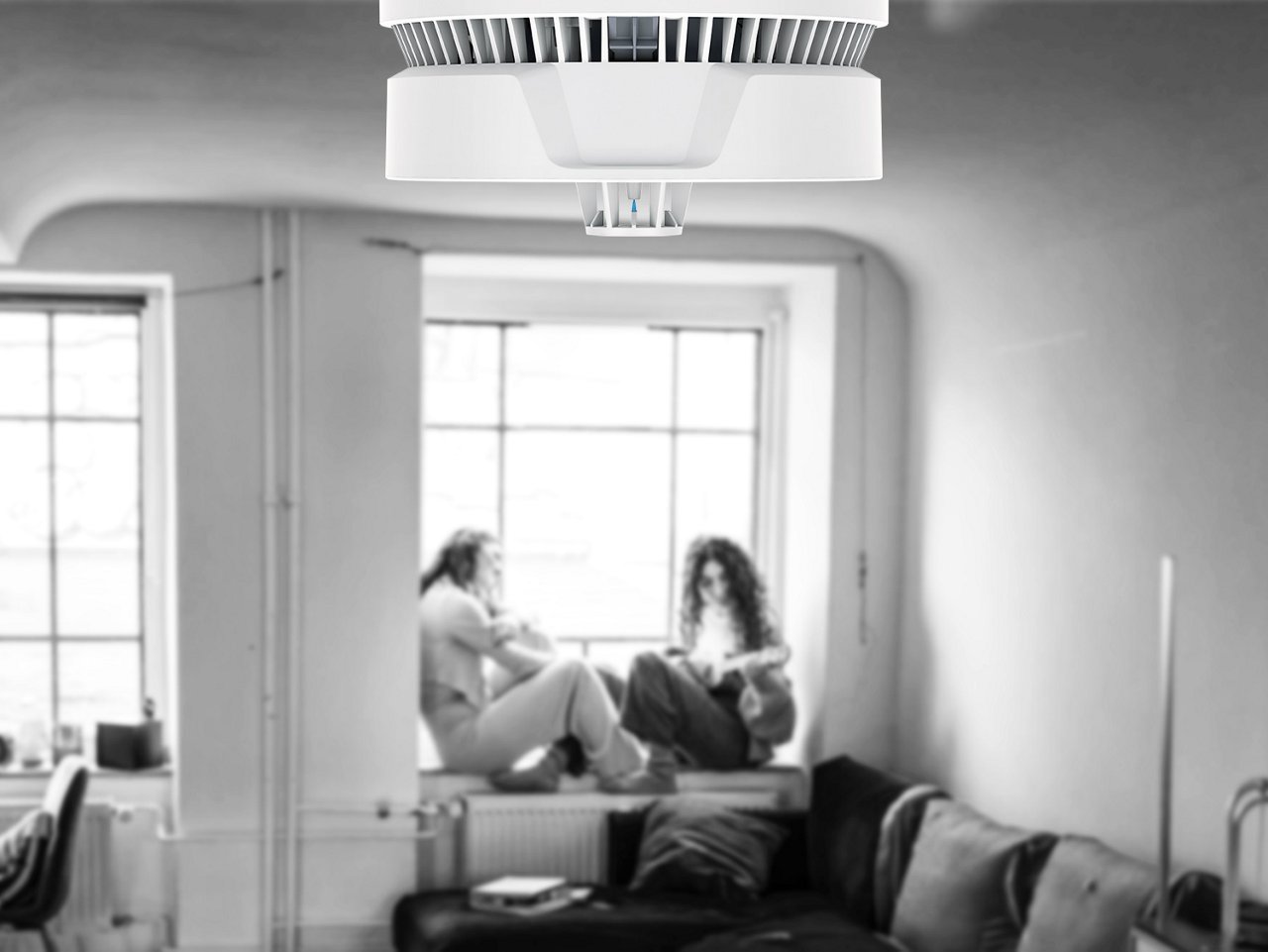 Zwei junge Frauen sitzen in ihrer Wohnung auf der Fensterbank und der Multisensor Plus ist im Vordergrund an der Decke montiert