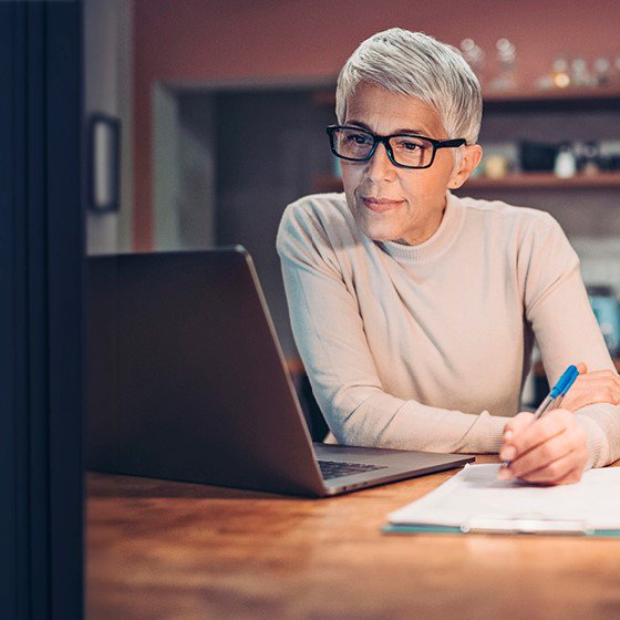 Frau mit grauen, kurzen Haaren und Brille sitzt vor Laptop