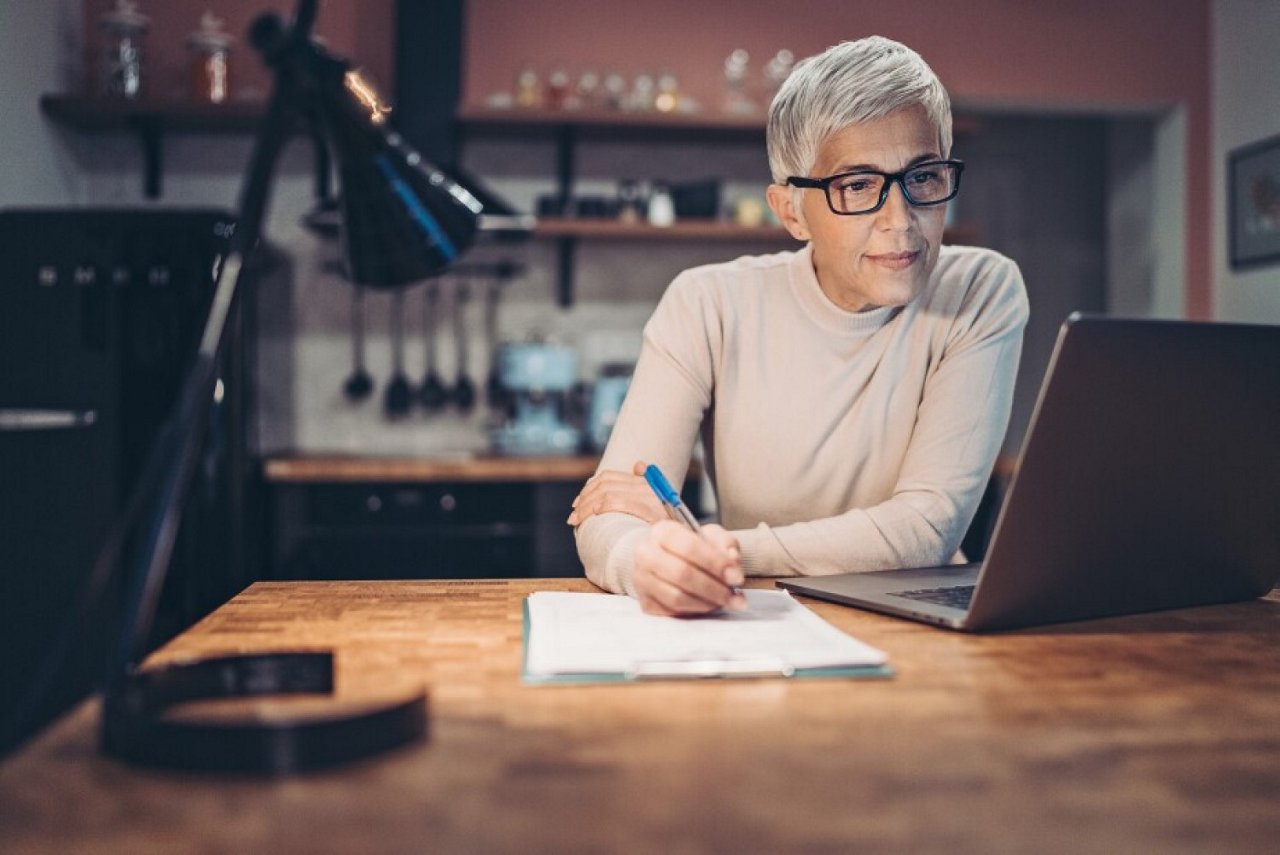 Ältere Frau arbeitet konzentriert am Laptop in der Küche