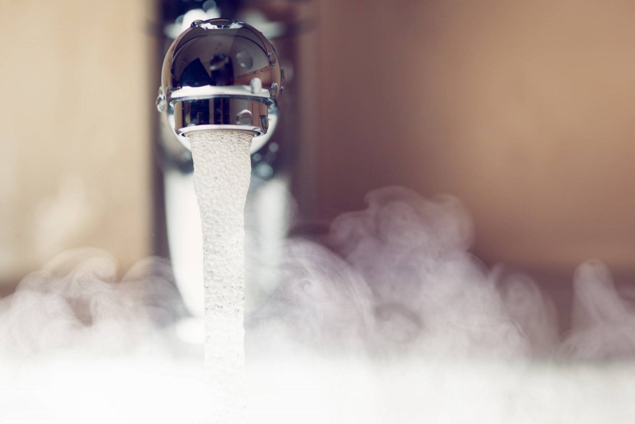 Nahaufnahme eines Wasserhahns mit fließendem heißen Wasser und aufsteigendem Dampf 