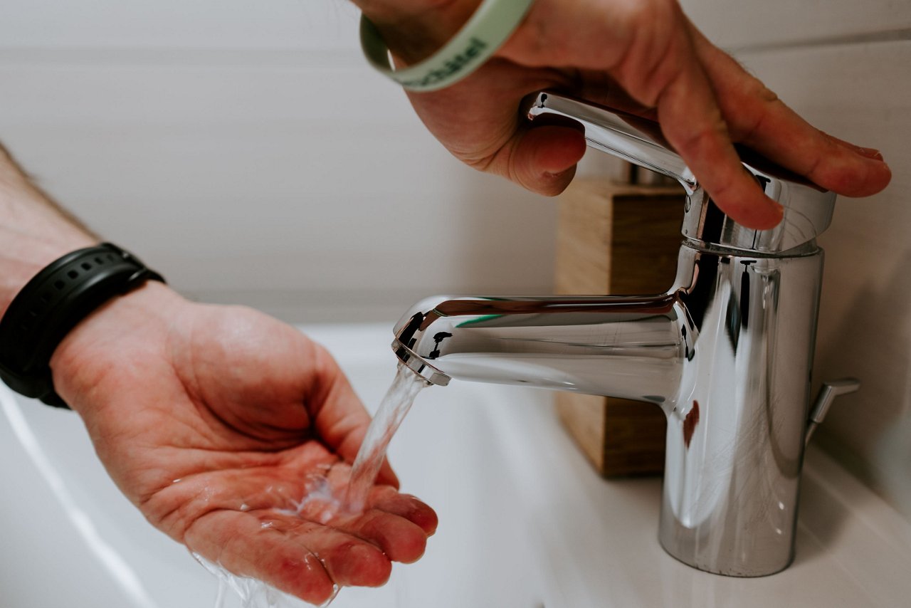 Eine Person hält ihre Hände unter einen Wasserhahn, während sie das Wasser aufdreht.