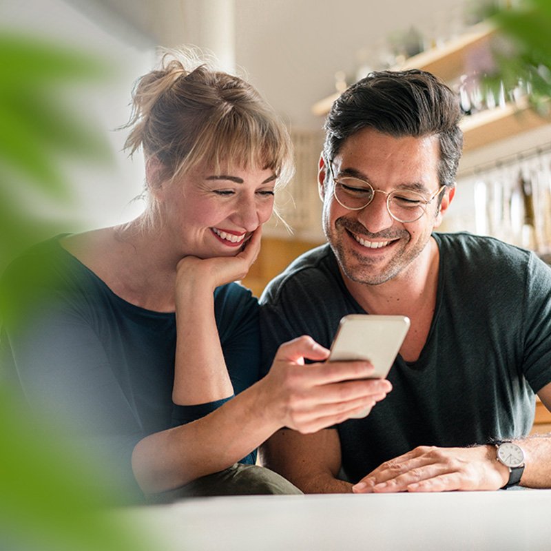 Mand og kvinde sidder i en lejlighed og kigger på en mobil.  