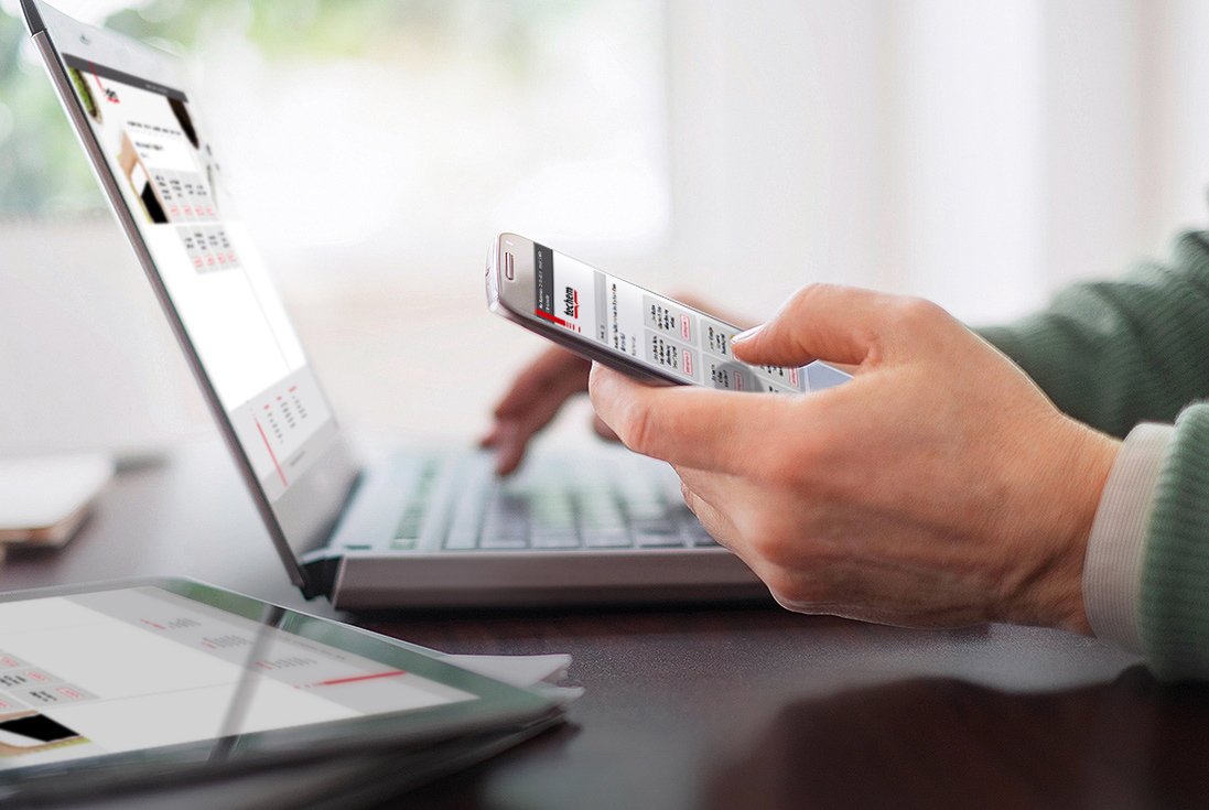 Person hält Smartphone mit geöffneter Webseite und tippt auf Laptop-Tastatur