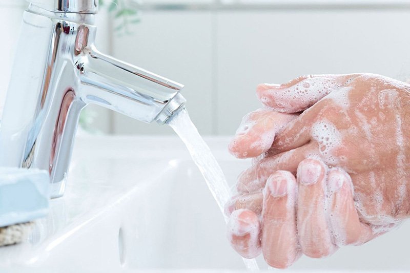 Hände werden mit Seife unter fliessendem Wasser gewaschen. Im Hintergrund ist ein weisses Badezimmer zu sehen.