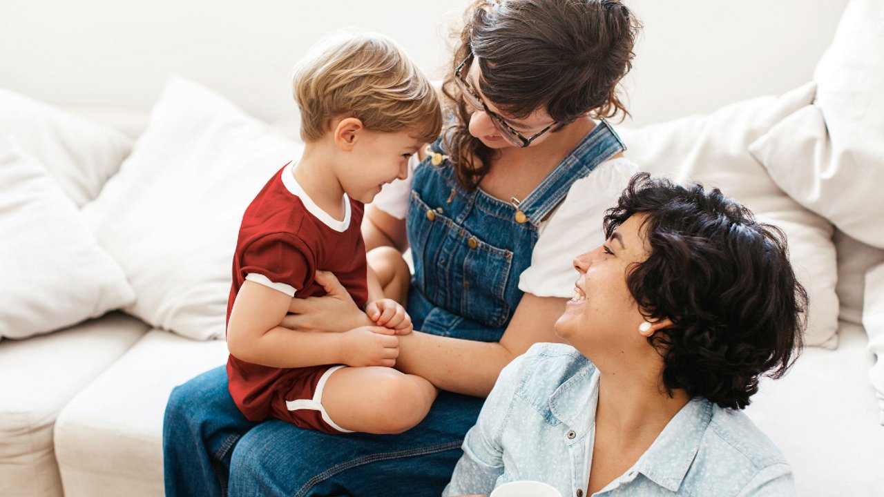 Zwei Frauen und ein Kind sitzen auf einem weißen Sofa und lachen