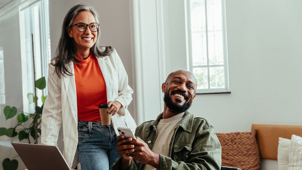 Eine Frau und ein Mann sitzen im Wohnzimmer vor dem Laptop und lachen