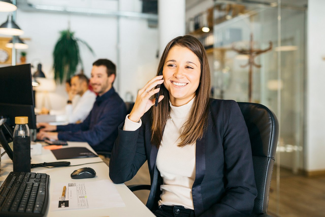 Smiling young woman talking on a smartphone in a office; Shutterstock ID 2087235706; purchase_order: TES 2140-001 ; job: Lizensierung Bildmaterial für Dorothea Heller 13-12-2021; client: Techem / faust & auge; other: 