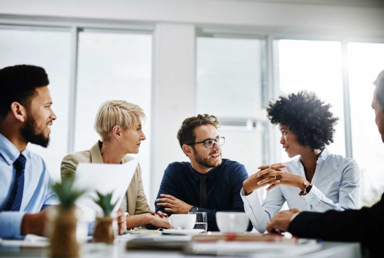 5 Personen sitzen entspannt an einem Tisch und halten eine Besprechung ab.