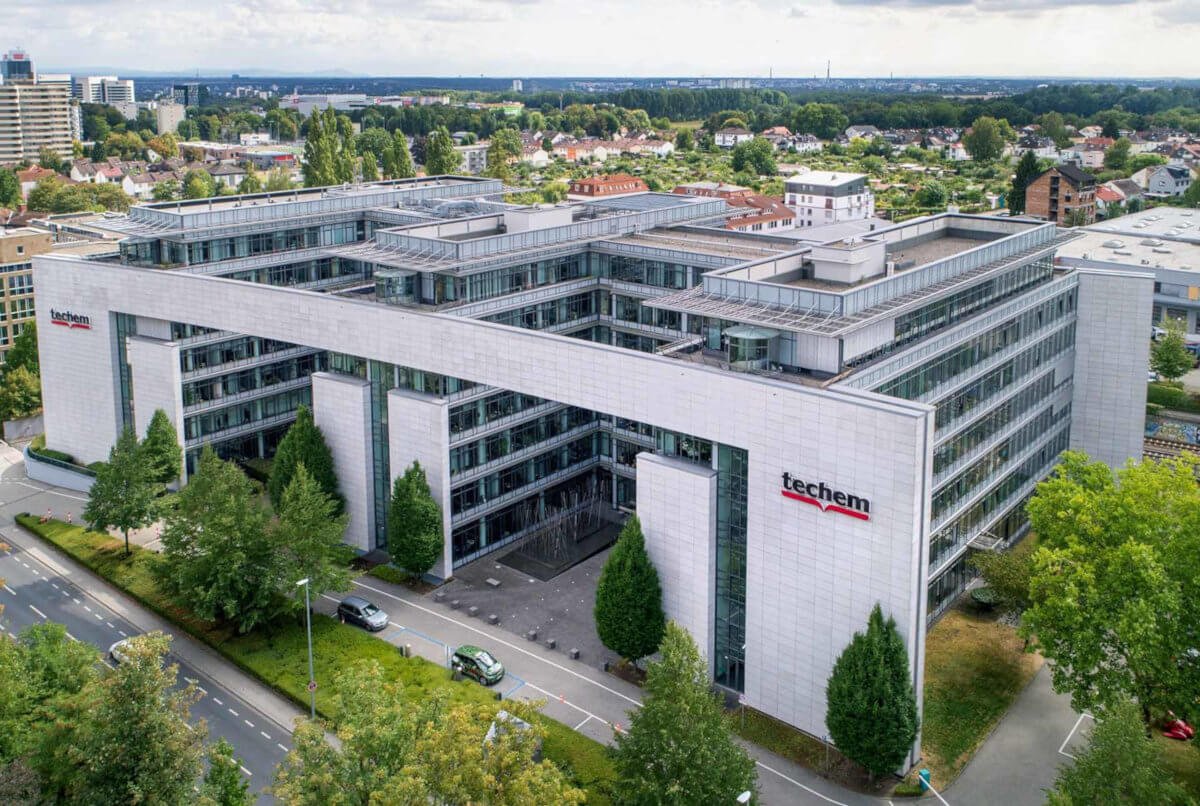 Techem Gebäude in Eschborn von oben aufgenommen. Im Hintergrund sieht man Eschborn. Das Gebäude ist umgeben von Bäumen.